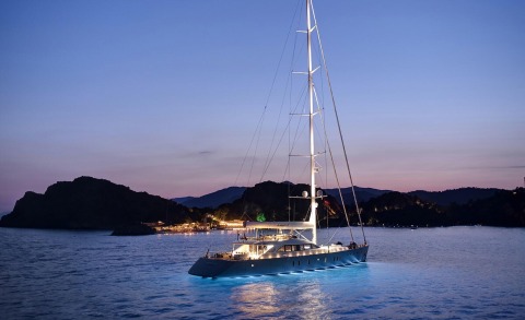 Nighttime view of a large yacht floating on water, with illuminated blue hull lighting and tall mast