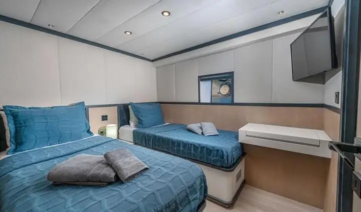 Twin cabin with two single beds, each with blue bedspreads and beige headboard, wall artwork, and ensuite doorway