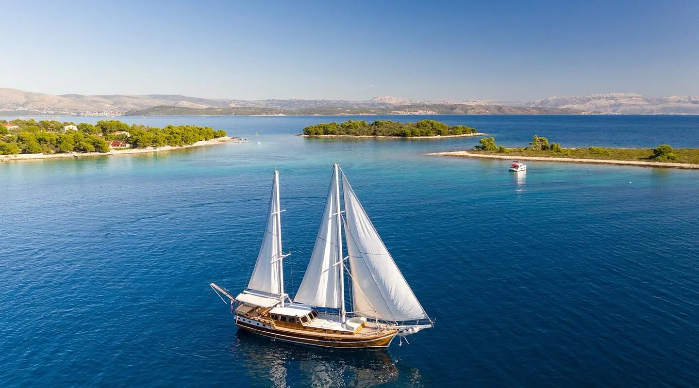 Andi Star yacht sailing in a calm blue harbor with white sails unfurled
