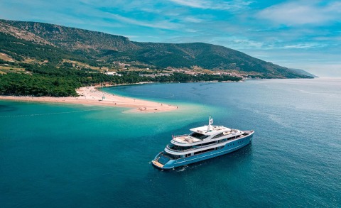 Ohana yacht cruising turquoise waters near a sandy beach with mountains in the background