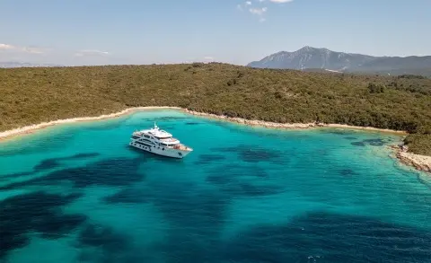 Olimp motor yacht anchored in turquoise waters near a rocky shore