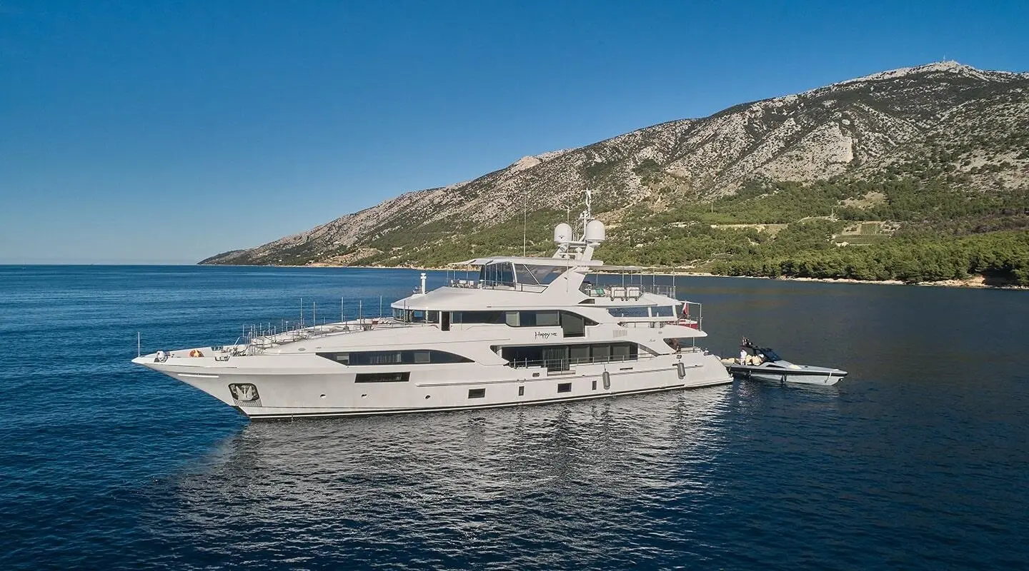 Luxurious white yacht named Happy Me anchored in calm blue bay with rocky coastline