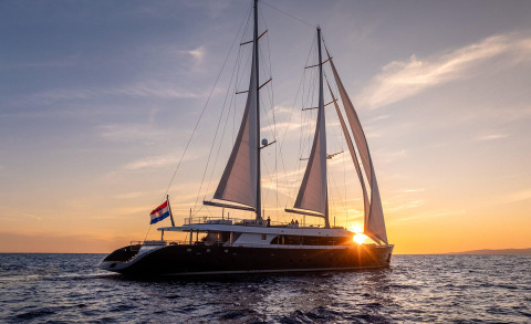 Two-masted sailing yacht near the sunset on the sea, people on deck