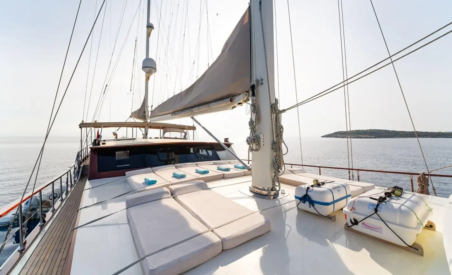 View from a yacht deck at sunset with sails, railing, and calm water