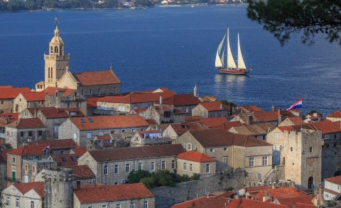 Coastal town with red-tiled roofs near blue sea and a sailing boat