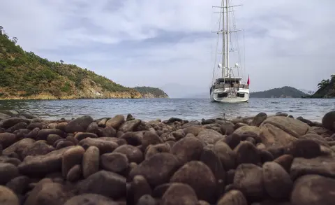 Sailboat anchored near rocky shore with hills in background