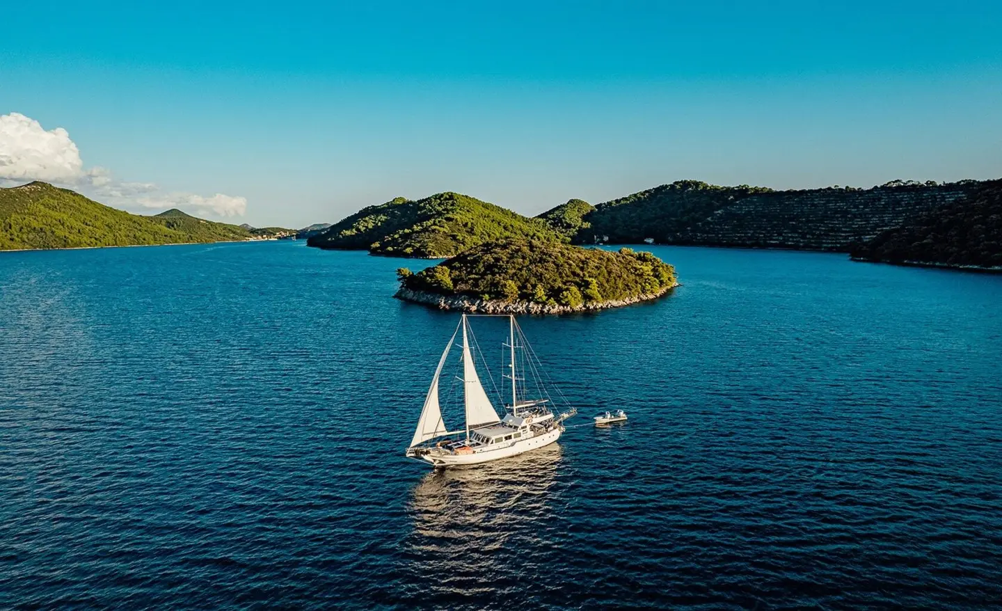Maske yacht sailing near rocky islets at sunset on calm blue water