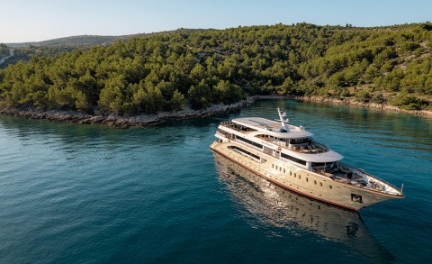 Luxurious yacht anchored in a blue-green coastal bay with green trees around