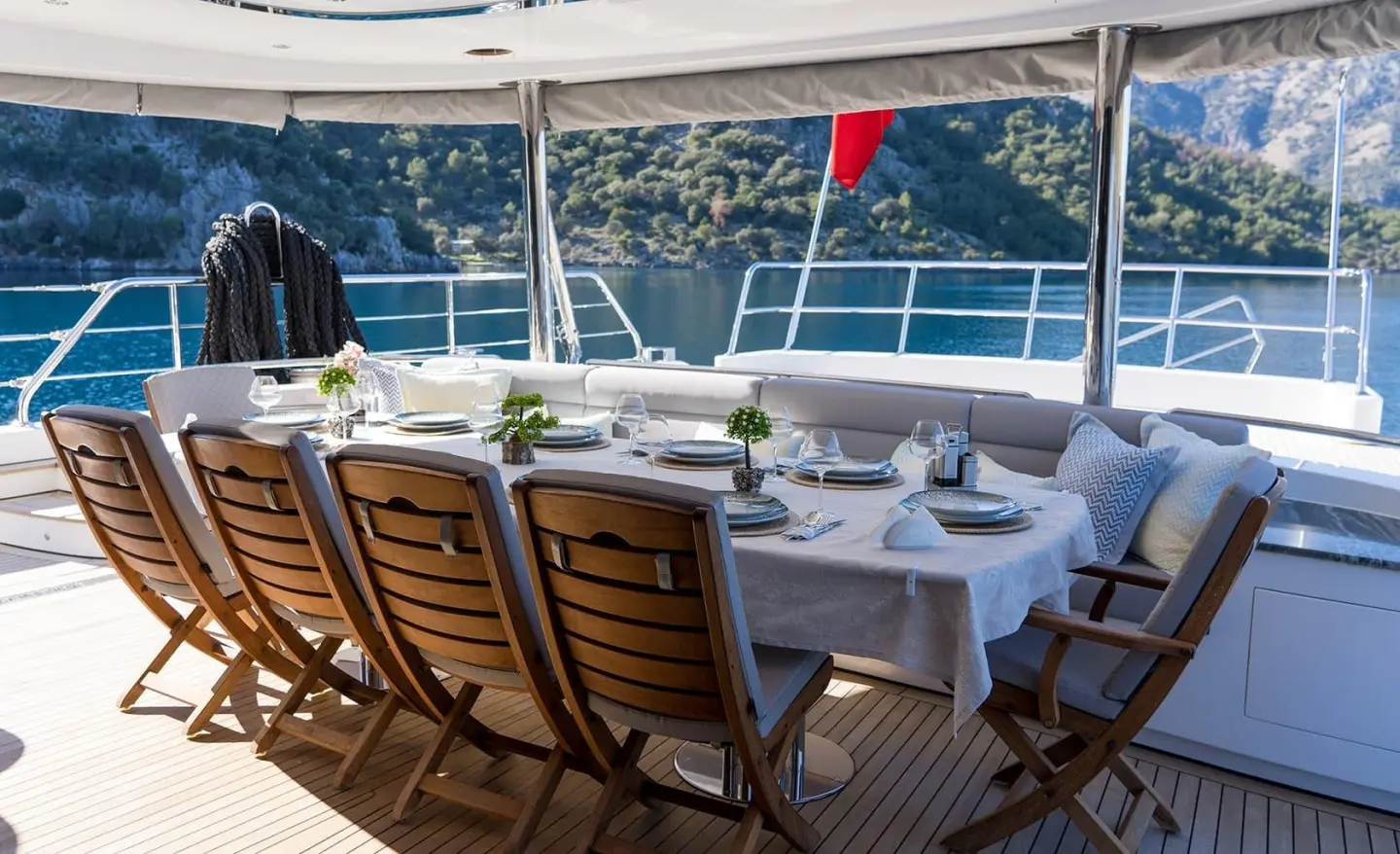 Sunlit aft dining on deck with wooden folding chairs and sea view