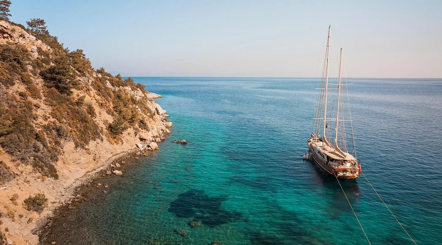 La Bella Vita yacht anchored near rocky coastline at sunset with clear blue water