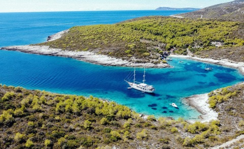 Corsario yacht anchored in a blue lagoon with green shrubs and rocky shore