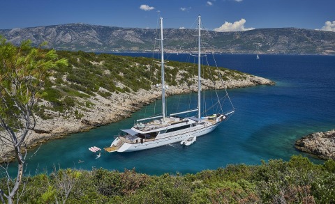 Two-masted yacht anchored in turquoise coastal water among rocky cliffs