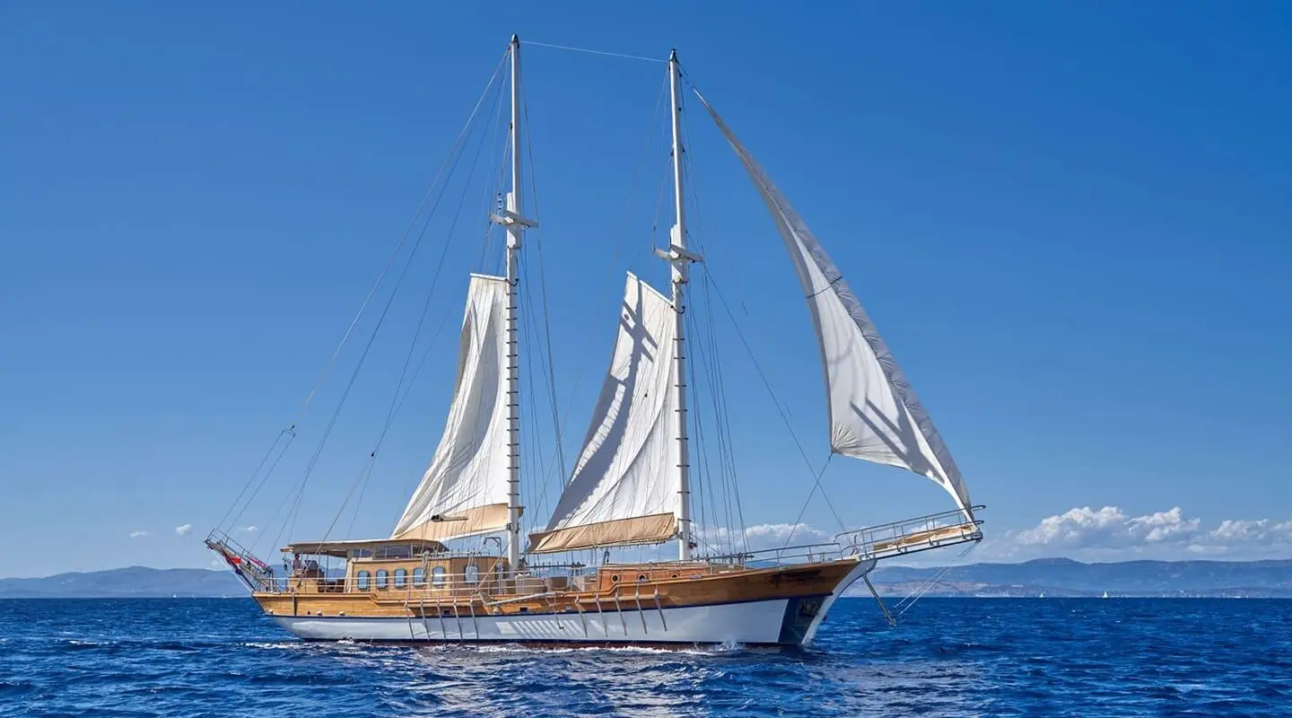 Elegant wooden gulet sailing yacht on the water with white sails and blue sky
