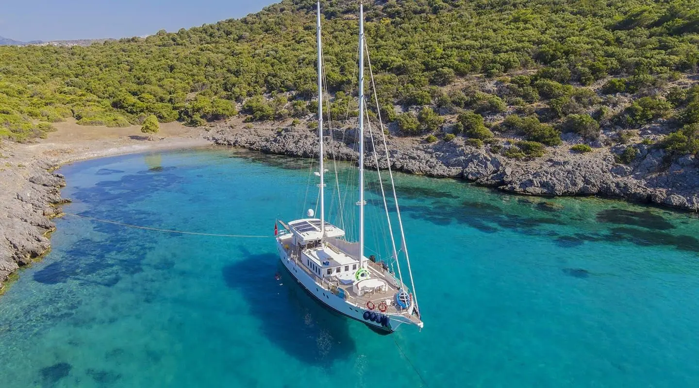 Gazella yacht anchored in clear blue water near rugged coast at sunset