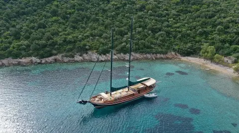 Gulet Ros Mare anchored in turquoise bay with forested hillside backdrop