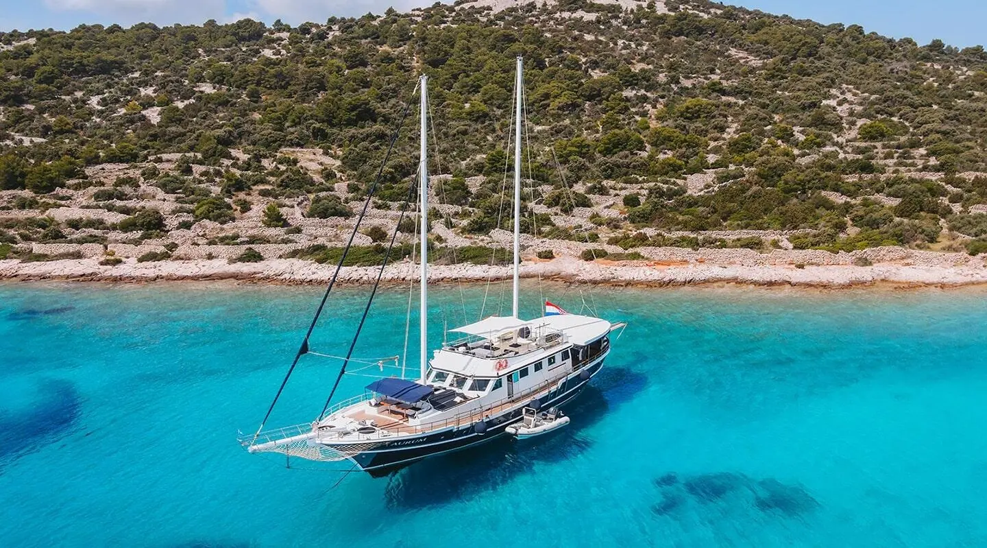 A white gulet named Aurum sails near a rocky coastline blue water
