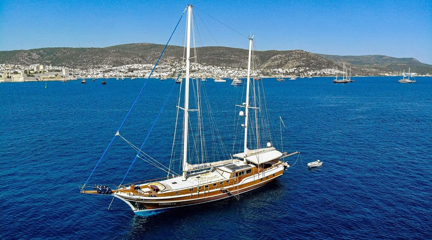 Enderim A sailing yacht moored in blue sea with a coastal town backdrop