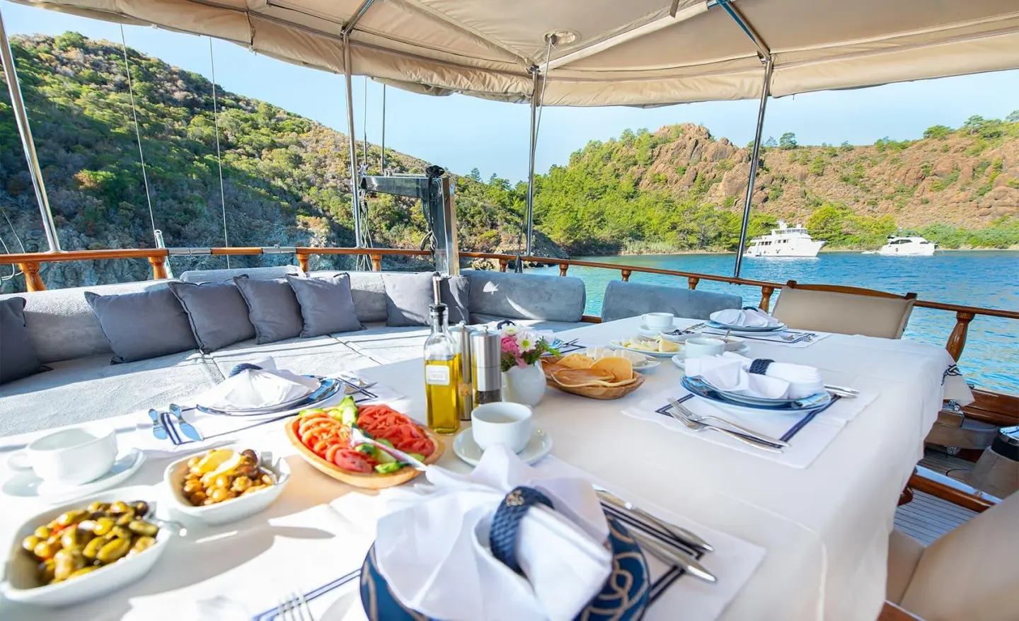 Ros Mare luxury yacht charter: sunlit deck with seating, cushions, and shaded area