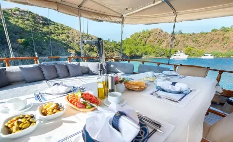 Ros Mare luxury yacht charter: sunlit deck with seating, cushions, and shaded area