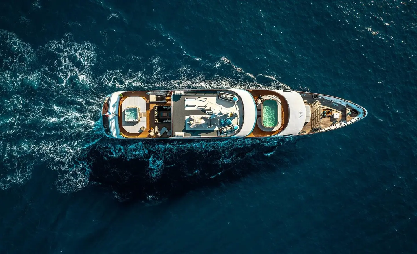 Top-down view of a luxury white yacht cruising deep blue sea at sunset