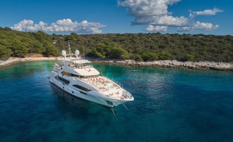 White motor yacht anchored in turquoise sea near rocky shoreline with trees