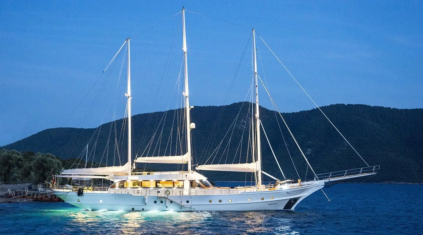 Yacht Bella Mare anchored near blue water with masts and hills in background