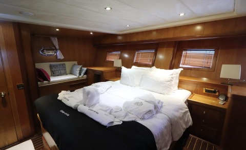 Interior of a yacht cabin with a large bed, wooden panels, and white linen