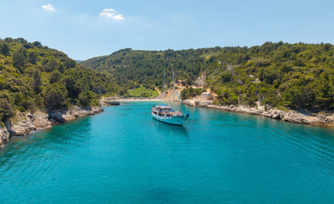 Mendula yacht anchored in turquoise sea between rocky green cliffs, two-masted gulet