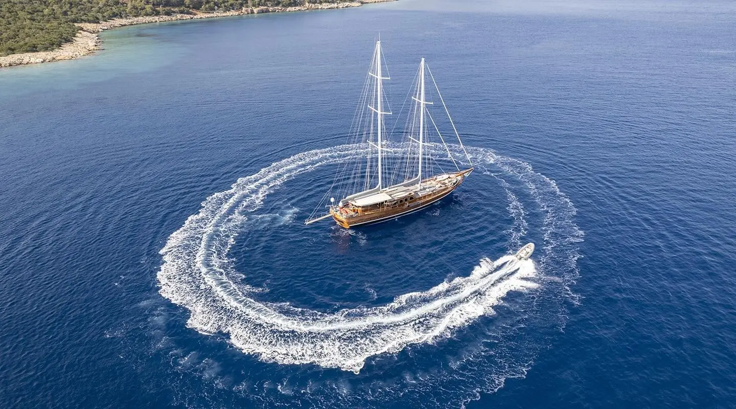 Two-masted gulet yacht sailing on blue sea forming a circular wake