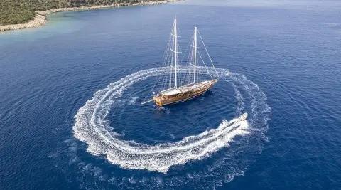 Two-masted gulet yacht sailing on blue sea forming a circular wake