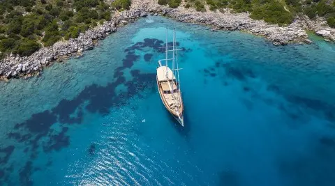 Wooden gulet yacht anchored in a clear blue bay with rocky shore nearby