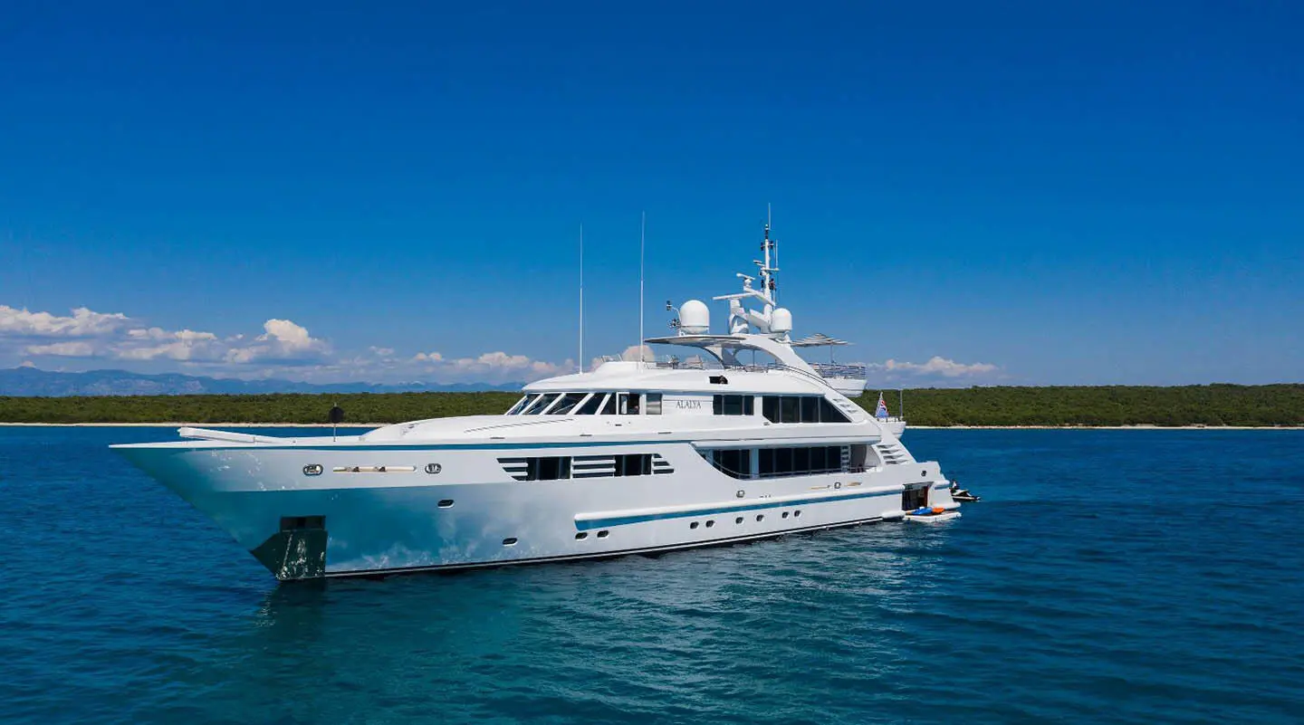 Alalya luxury motor yacht anchored offshore with clear blue water and a distant coastline