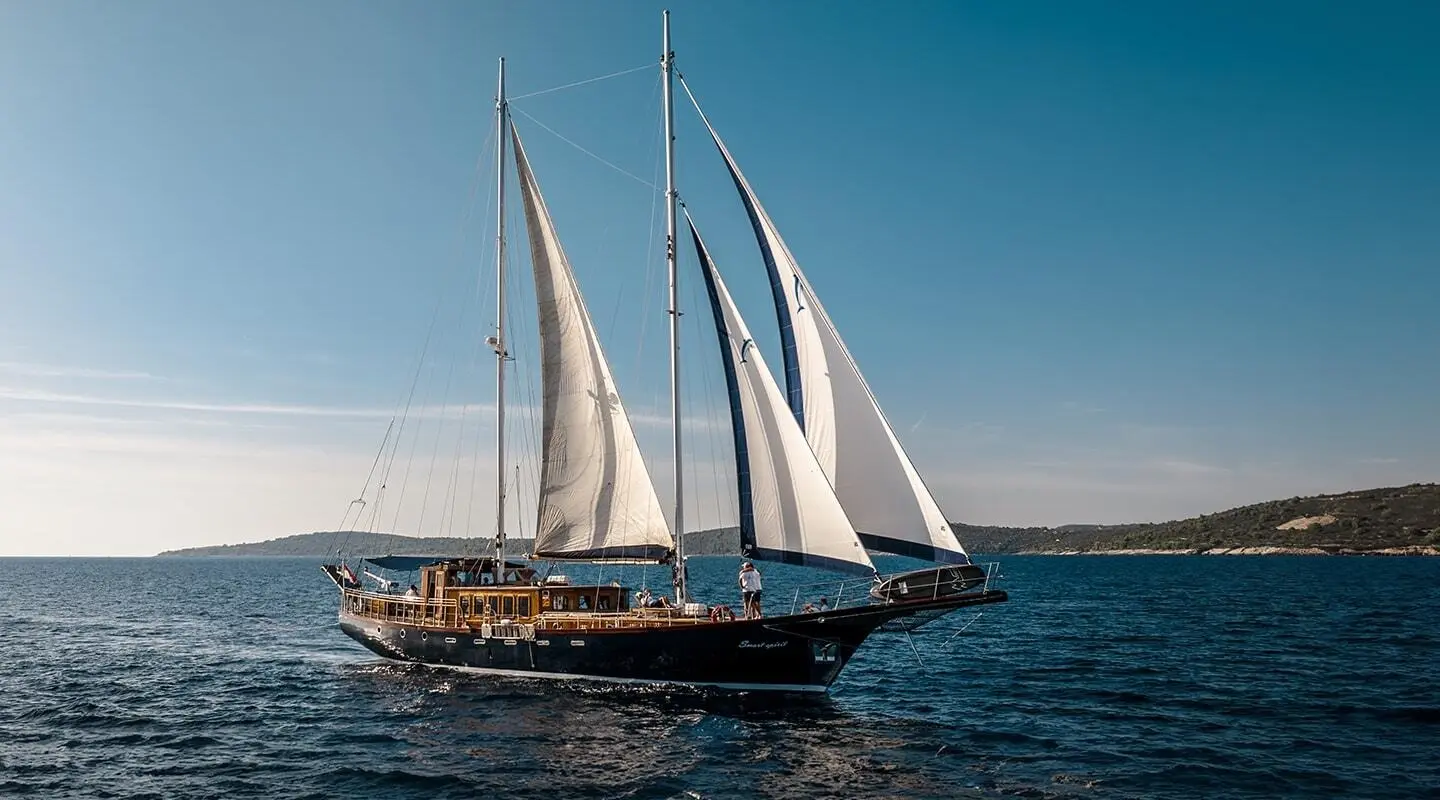 Smart Spirit yacht with multiple sails billowing on calm blue sea at sunset