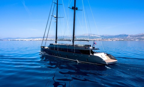 Scorpios luxury 52m sailing yacht cruising sapphire blue waters with a coastal town in the background