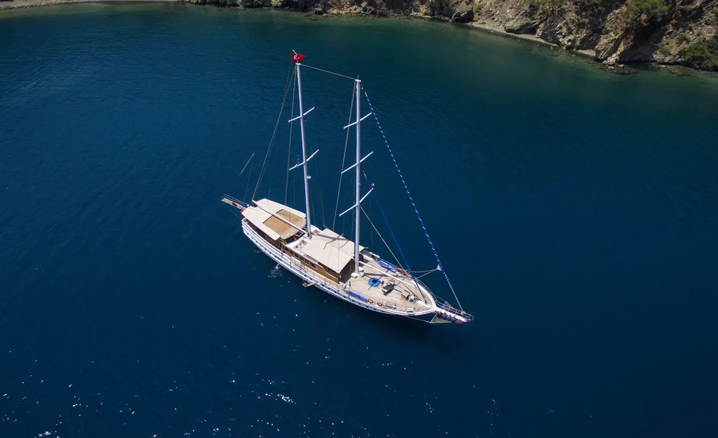 Two-masted sailboat anchored in blue sea near rocky shore