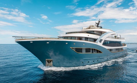 Blue yacht with white superstructure sails in open sea, bow and upper deck visible