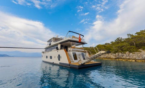 Simay M yacht viewed from water with clear sky and rocky shore in background