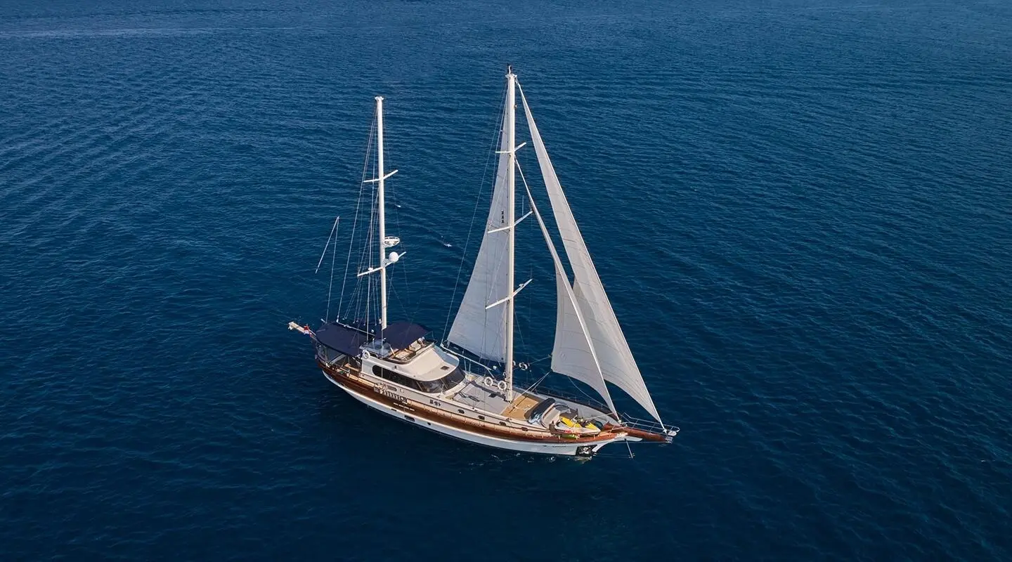 A gulet-style yacht named Lotus sails on calm blue water with two masts