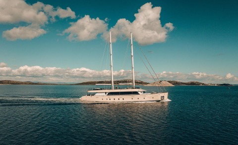Two-masted luxury sailing yacht cruising on calm blue sea with rocky islands in the background