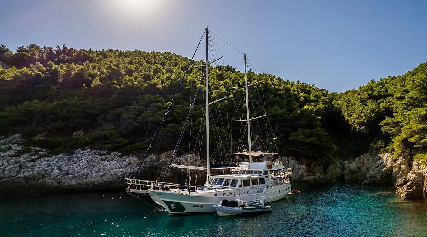 Maske yacht moored in turquoise cove with rocky hillside backdrop at sunset