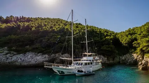 Maske yacht moored in turquoise cove with rocky hillside backdrop at sunset