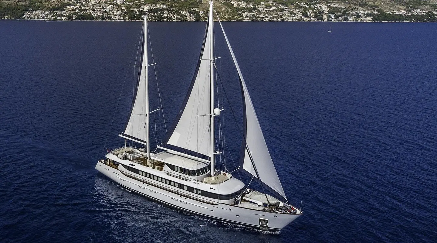Omnia luxury sailing yacht gliding on blue sea with sails up near coastline