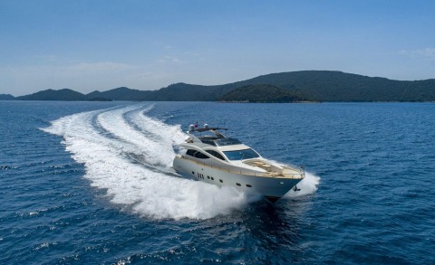 White yacht speeding across blue sea with distant hilly coastline in the background