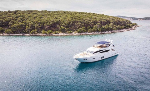 White luxury yacht with shaded upper deck near tree-covered coastline