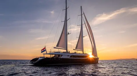 Nocturno luxury sailing yacht at sunset, two masts, dark hull, serene open sea panorama
