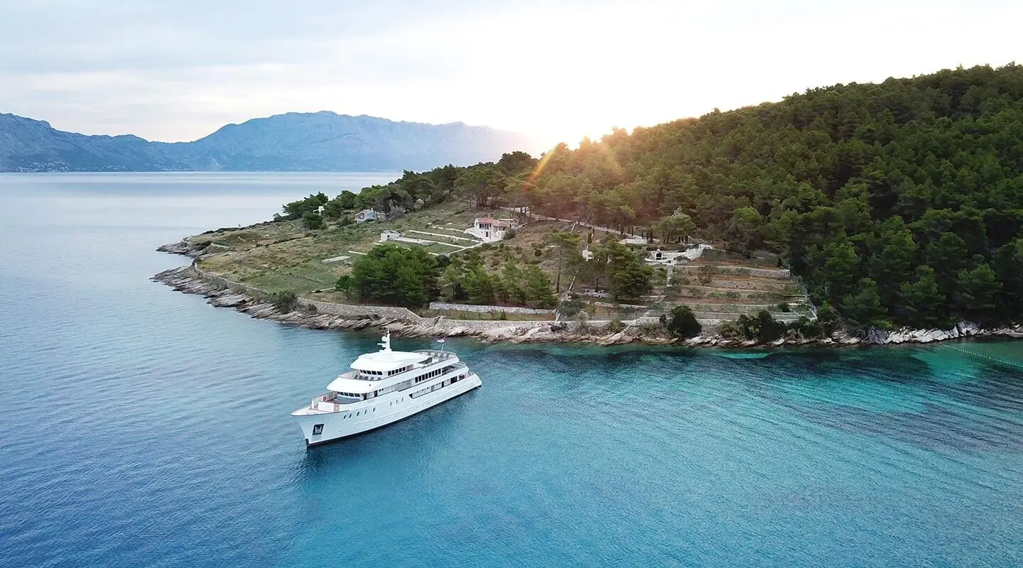 Yolo yacht anchored near turquoise water, rocky coastline and shore town