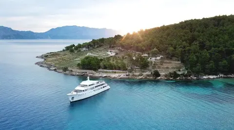 Yolo yacht anchored near turquoise water, rocky coastline and shore town