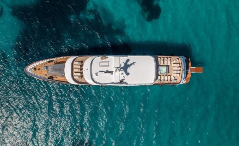 Top-down view of the Olimp yacht on turquoise water, sunbathing areas on the stern and deck details