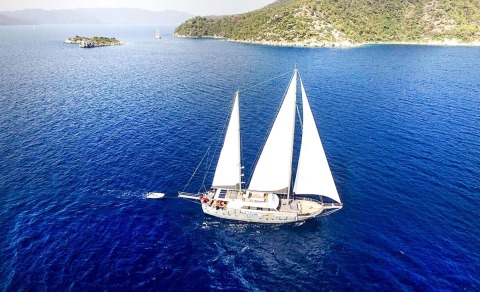 White sailing yacht on blue sea with rocky coastline in the background