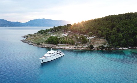 Yolo yacht anchored near a tree-covered hillside on clear blue waters